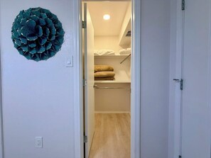 Ein Durchgang zu einem Zimmer mit einem Bett, einer Ablage mit zusammgefalteten Decken und einer Wandleuchte.