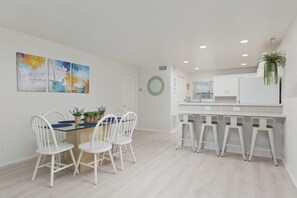 A modern kitchen with white cabinets, a bar area with stools, and a dining table with chairs. - Casa Sol Azul 1A - Cozy 2BR, Ground Floor, Pool! (South Padre Island)