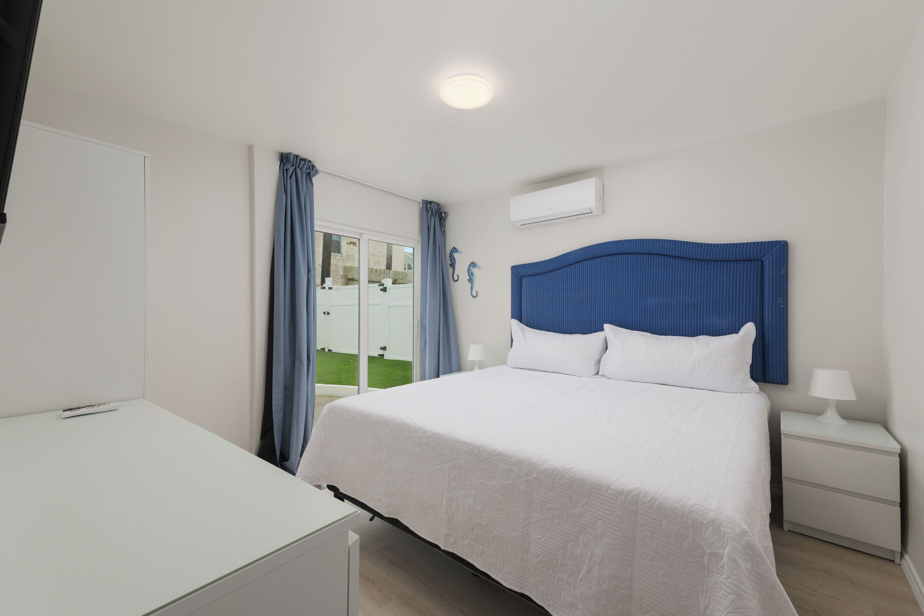 Een hotelkamer met een bed, een bureau, een nachtkastje, een lamp en een airconditioningsysteem.