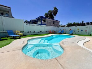 A swimming pool with a curved edge, surrounded by a concrete deck. There are lounge chairs and a white fence with floral decorations. - Casa Sol Azul 2A - Spacious 2BR, Pool! (South Padre Island)