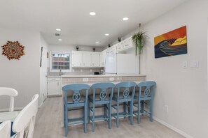 A modern kitchen with white cabinets, a white refrigerator, and a blue bar stool seating area. - Casa Sol Azul 2A - Spacious 2BR, Pool! (South Padre Island)
