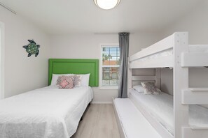 Ein Schlafzimmer mit einem Etagenbett, einem Einzelbett, einem grünen Kopfteil und einem Fenster mit Blick auf Gebäude.