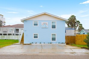 Une maison à deux étages, avec une façade bleue, un porche à l’avant et un petit jardin.