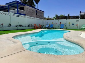 A swimming pool with a curved edge, surrounded by a concrete deck. There are lounge chairs and a white fence with flower paintings. - Casa Sol Azul 2B - Quirky Loft, Pool! (South Padre Island)