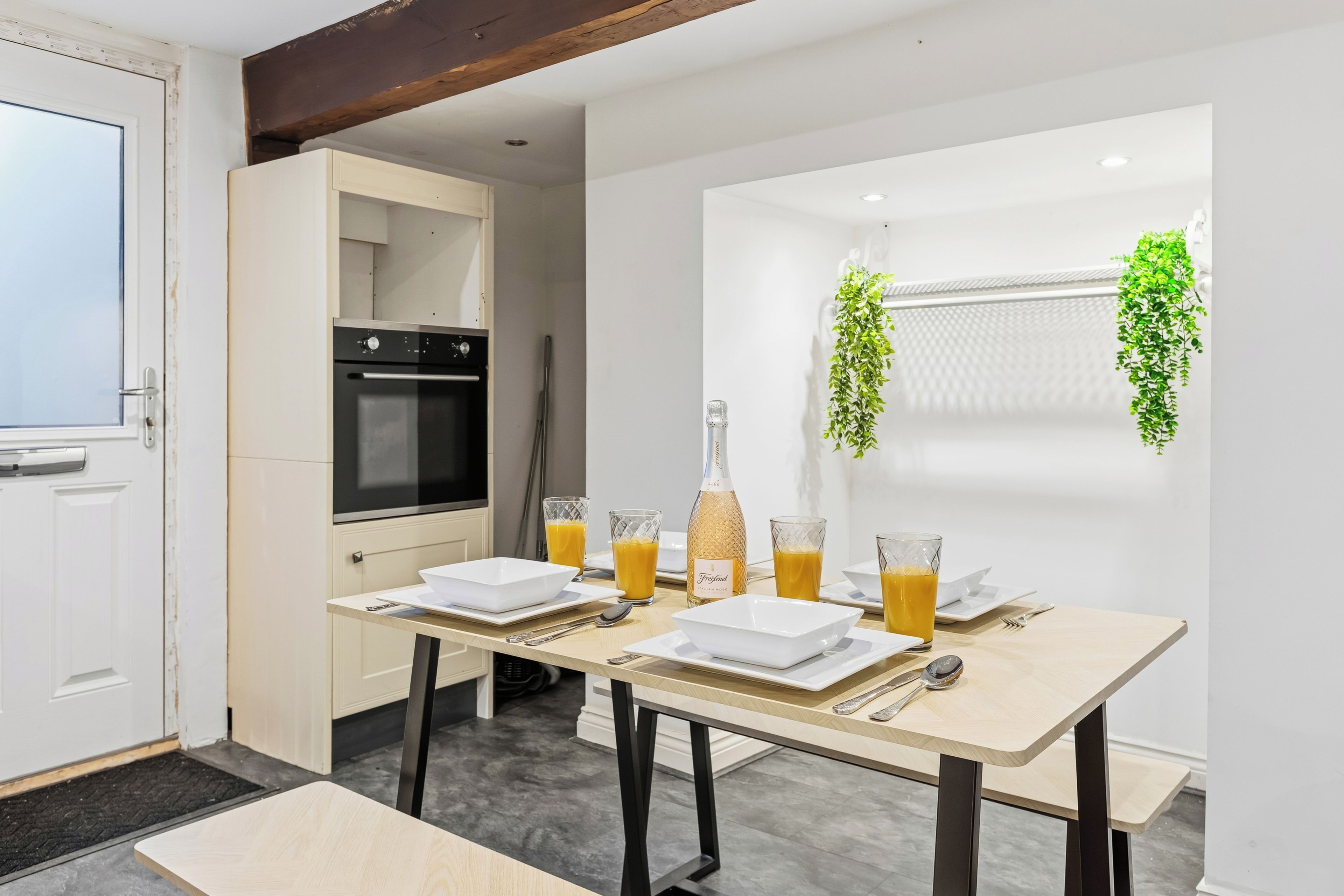 A modern kitchen with a dining table set for breakfast, including a bottle of Italian wine and glasses of orange juice.