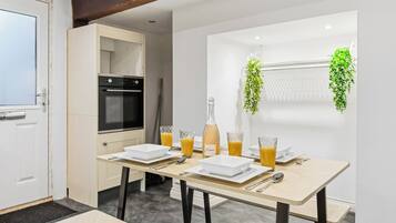A modern kitchen with a dining table set for breakfast, including a bottle of Italian wine and glasses of orange juice.