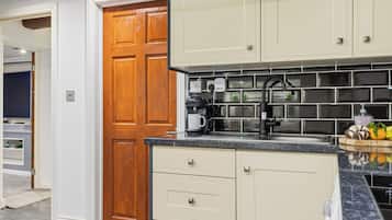 A kitchen with a wooden door, white cabinets, a black faucet, and a countertop with a coffee maker and fruits.