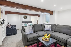 A modern living room with a sectional sofa, a coffee table with fruit and a drink, and a bed in the background. - The Cozy Snug Basement, Sleeps 2 in Bury (Bury)