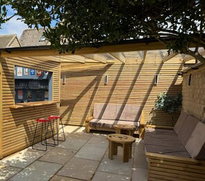 A wooden deck with a bar area, seating, and a small table. - Maple Cottage Bourton (Bourton-on-the-Water)