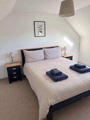 A neatly made bed with a headboard, two bedside tables with lamps, and a framed picture on the wall. - Maple Cottage (Bourton-on-the-Water)