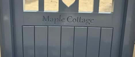 A grey metal gate with the words 'Maple Cottage' and a heart-shaped cutout.