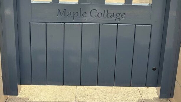 Una reja metálica gris con la inscripción 'Maple Cottage' y un corte en forma de corazón.