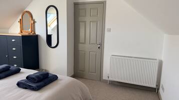 Un dormitorio con cama, cómoda, espejo, puerta y radiador.