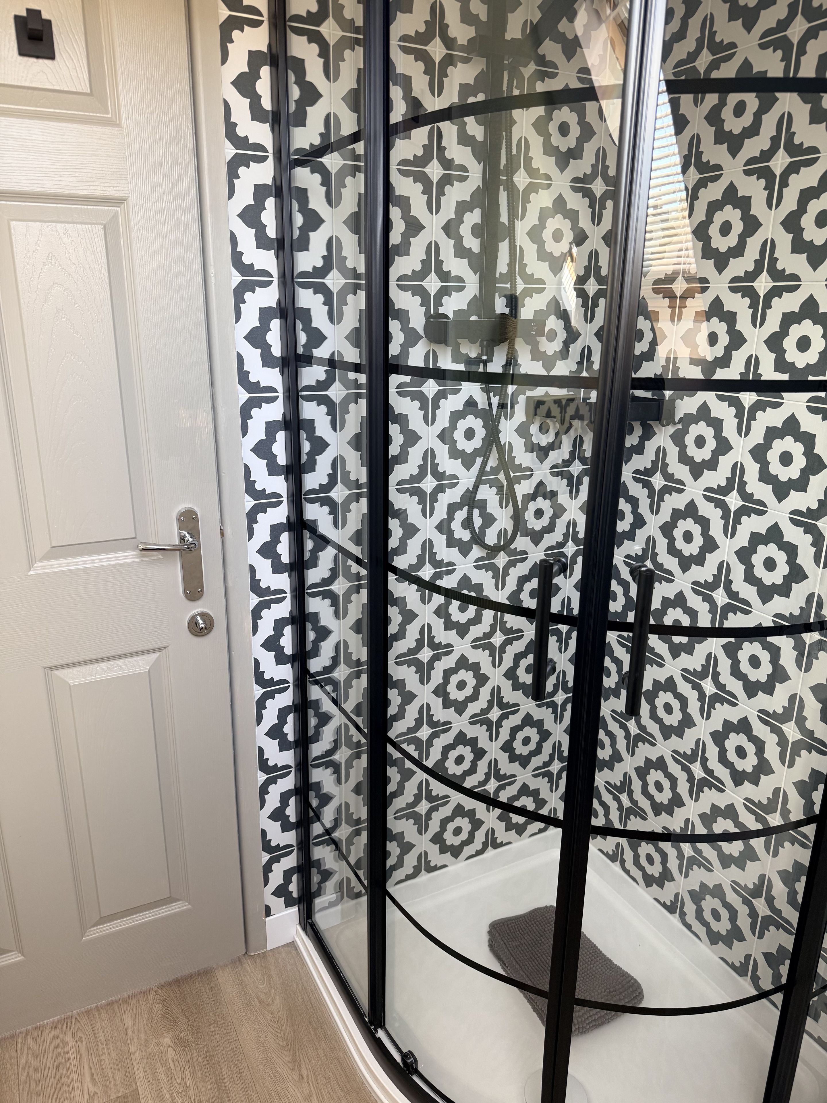 A shower enclosure with a black frame and patterned tiles.