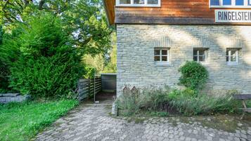 A stone building with a wooden upper section, a metal gate, and a paved path leading to a wooden bench.