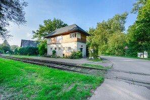 A two-story house with a stone facade, a wooden upper floor, and a visible railway track in the foreground.
