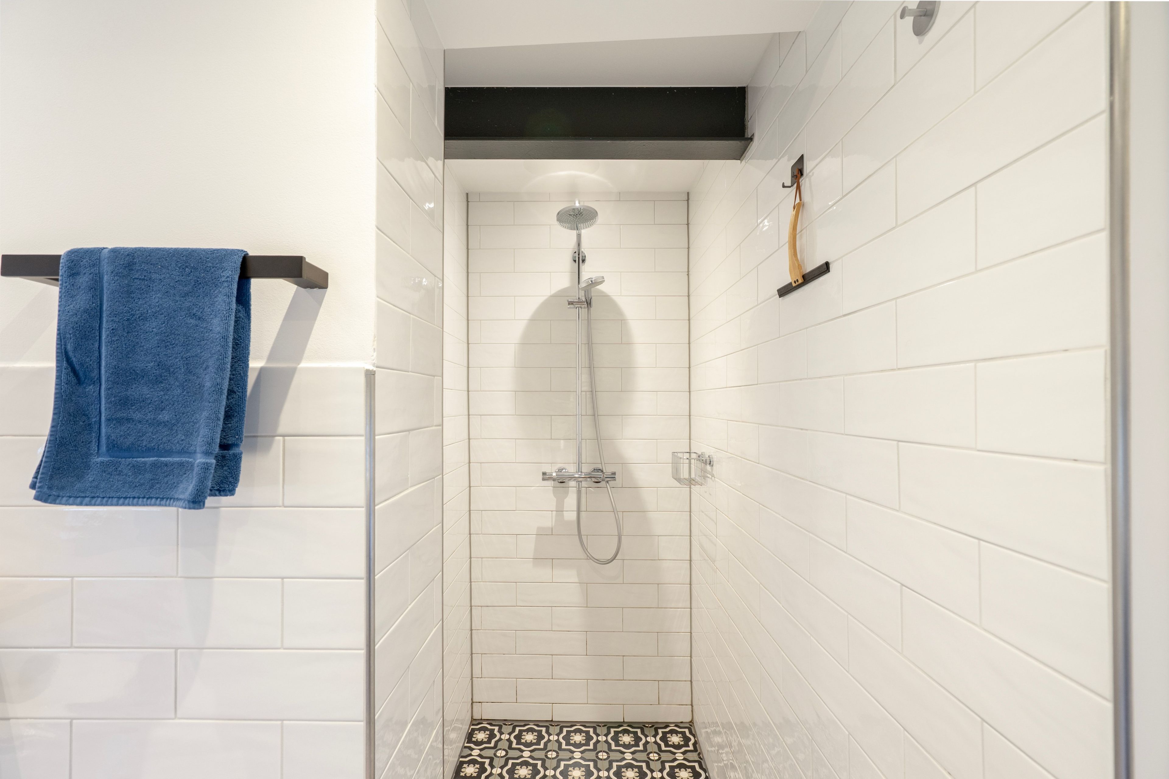 Un baño pequeño y estrecho con paredes de azulejos blancos y suelo de losetas negras.