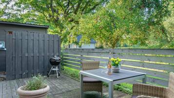 Eine Terrasse im Freien mit Tisch, Stühlen, einem Grill und einem Blumentopf.