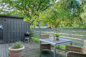 An outdoor patio with a table, chairs, a grill, and a potted plant.