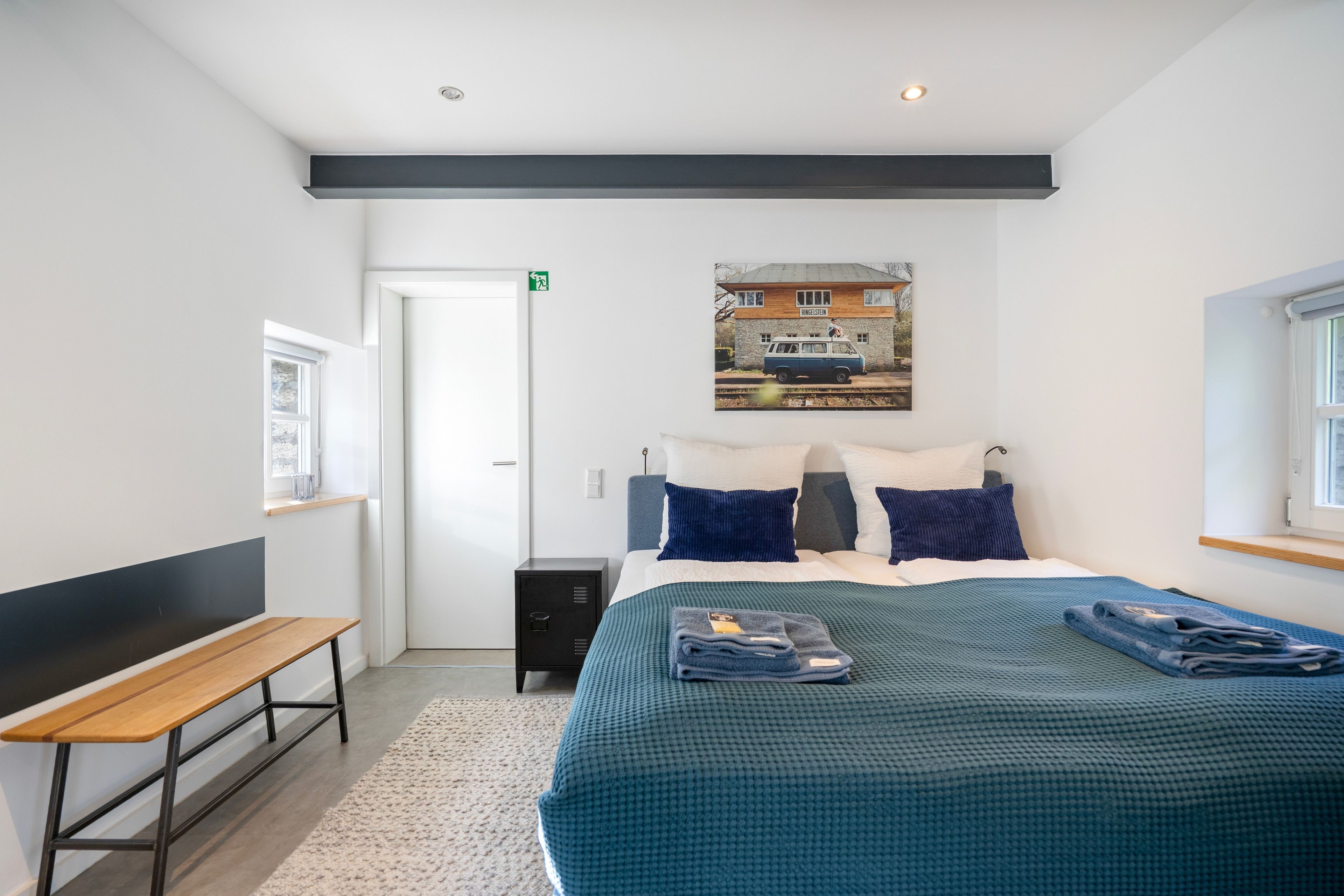 Ein Hotelzimmer mit einem Bett, einer Sitzbank, einer kleinen Kommode und einem Bild an der Wand.