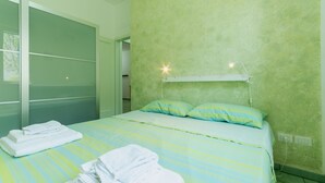 Una habitación de hotel con una cama, almohadas, una mesita de noche, una lámpara y un estante en la pared.