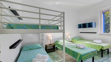 A dormitory room with bunk beds, two single beds, a window with a view, and a small table with a lamp.