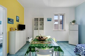 A compact dining area with a table, chairs, a television, and a refrigerator.