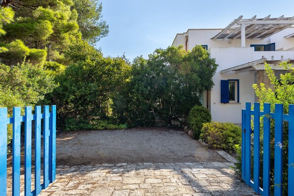 A paved driveway leading to a building with a white facade and blue shutters.