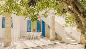 Un patio con una mesa y sillas blancas, contraventanas azules y una escalera.