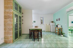 A compact kitchen with a dining table and chairs, a refrigerator, a microwave, and a small cabinet.