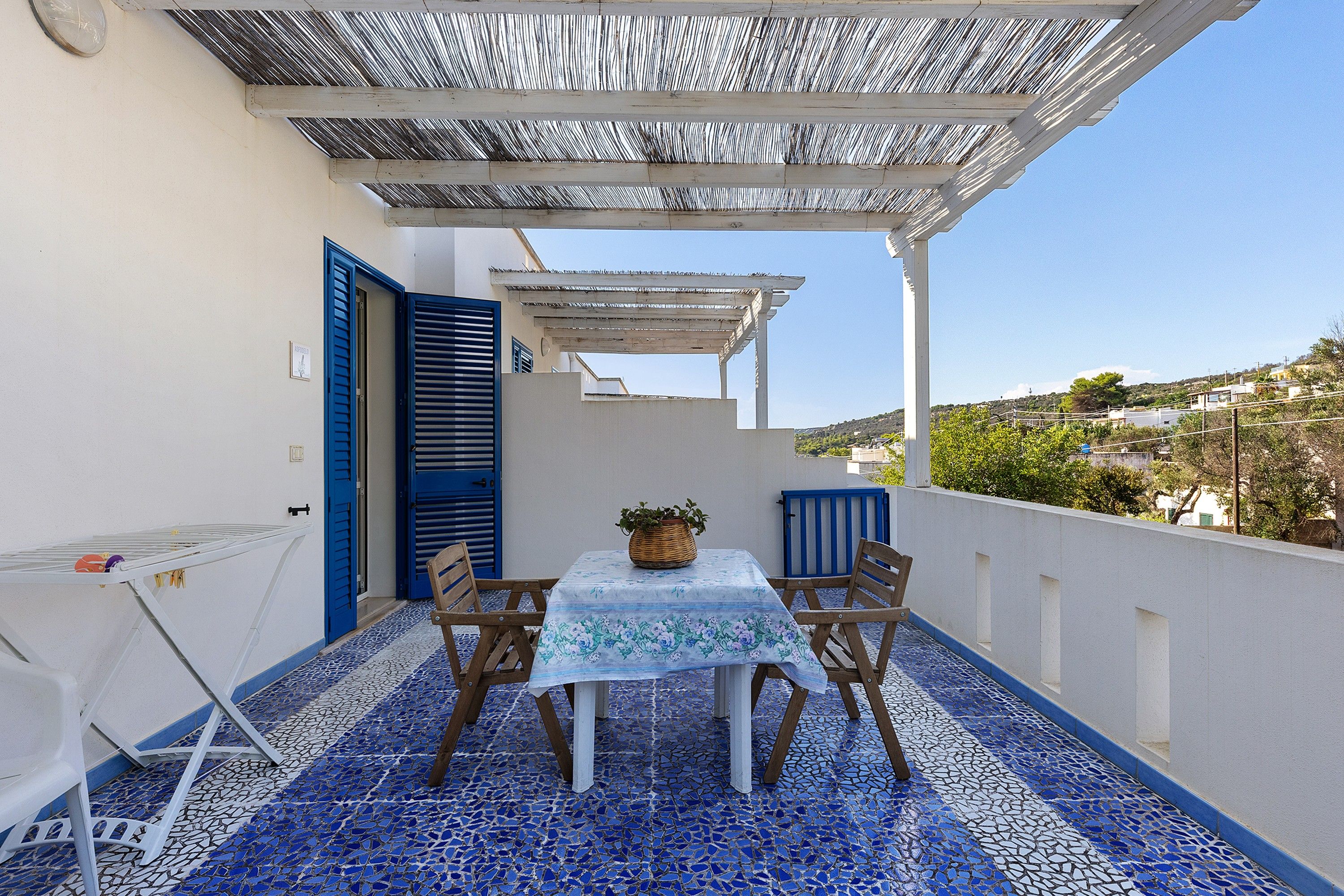 A terrace with a table and chairs, a potted plant, and a view of the landscape.