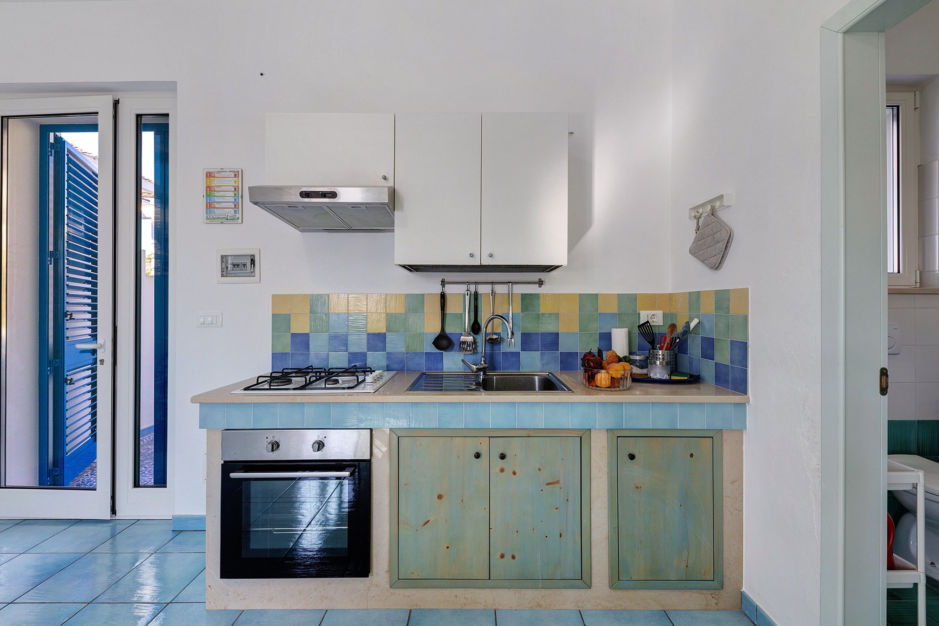 Una cucina compatta con piano cottura a gas, forno e rivestimento in piastrelle.