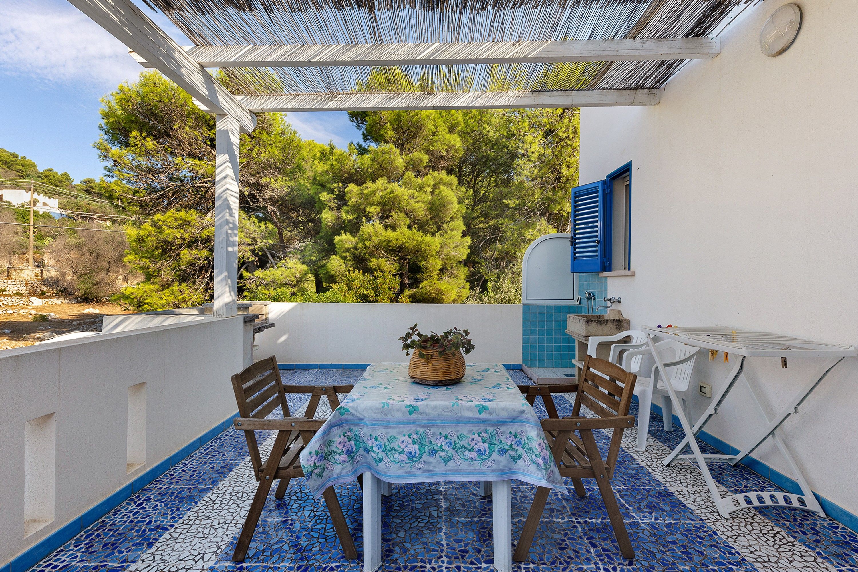 A patio with a table and chairs, a small sink, and a window overlooking trees.
