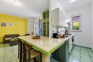Una cocina compacta con una isla central, una zona de comedor con sofá y un ventanal con vistas a zonas verdes.