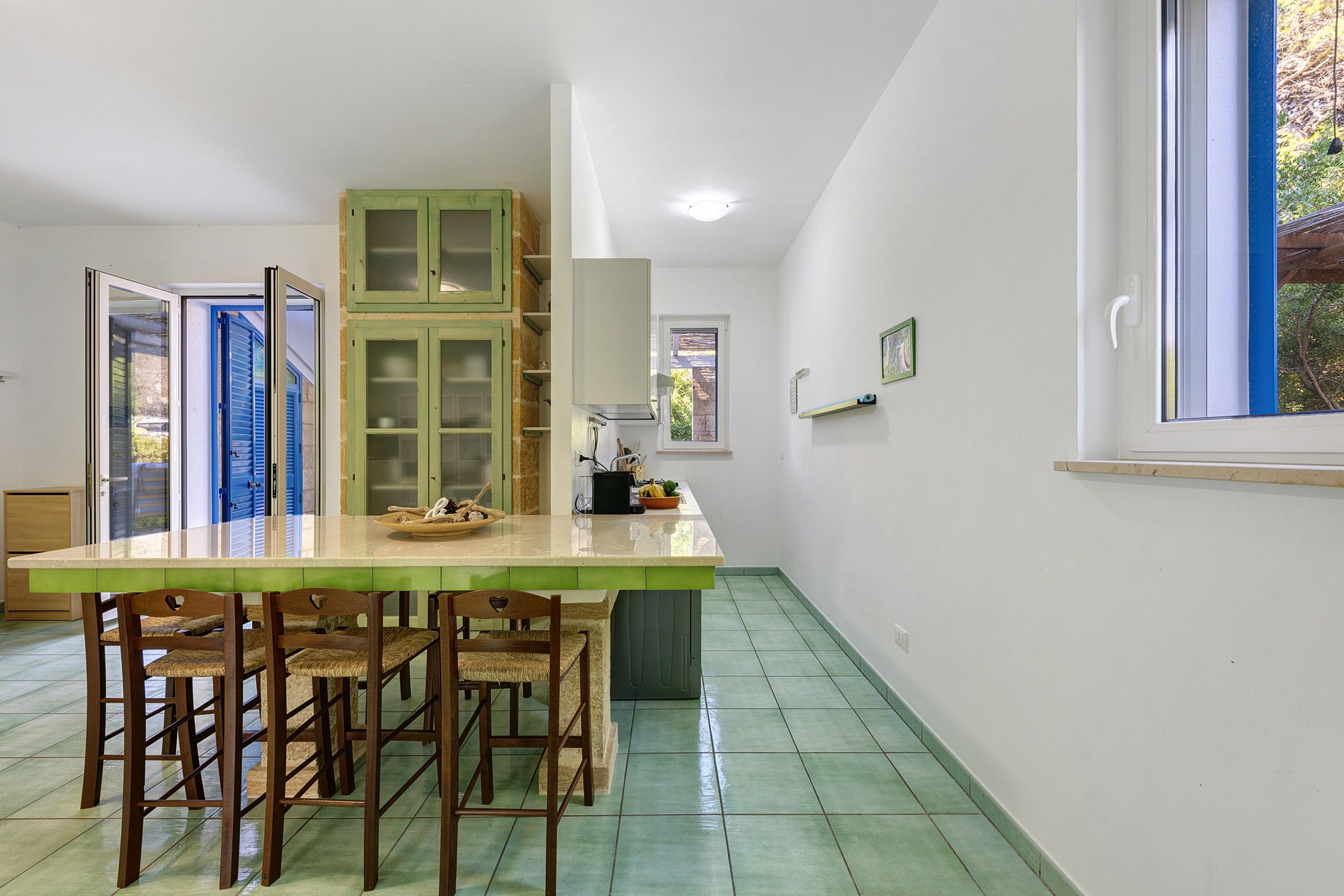 Una cucina con un'isola grande, sedie di legno, un tavolo da pranzo e una finestra con vista su spazi verdi.