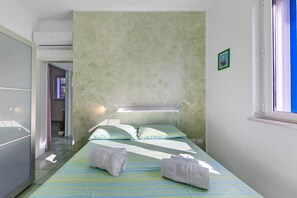 A bedroom with a bed, two towels, a bedside lamp, a picture frame, and a window.