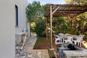 An outdoor patio with a stone pathway, a table and chairs, a grill, and a pergola.