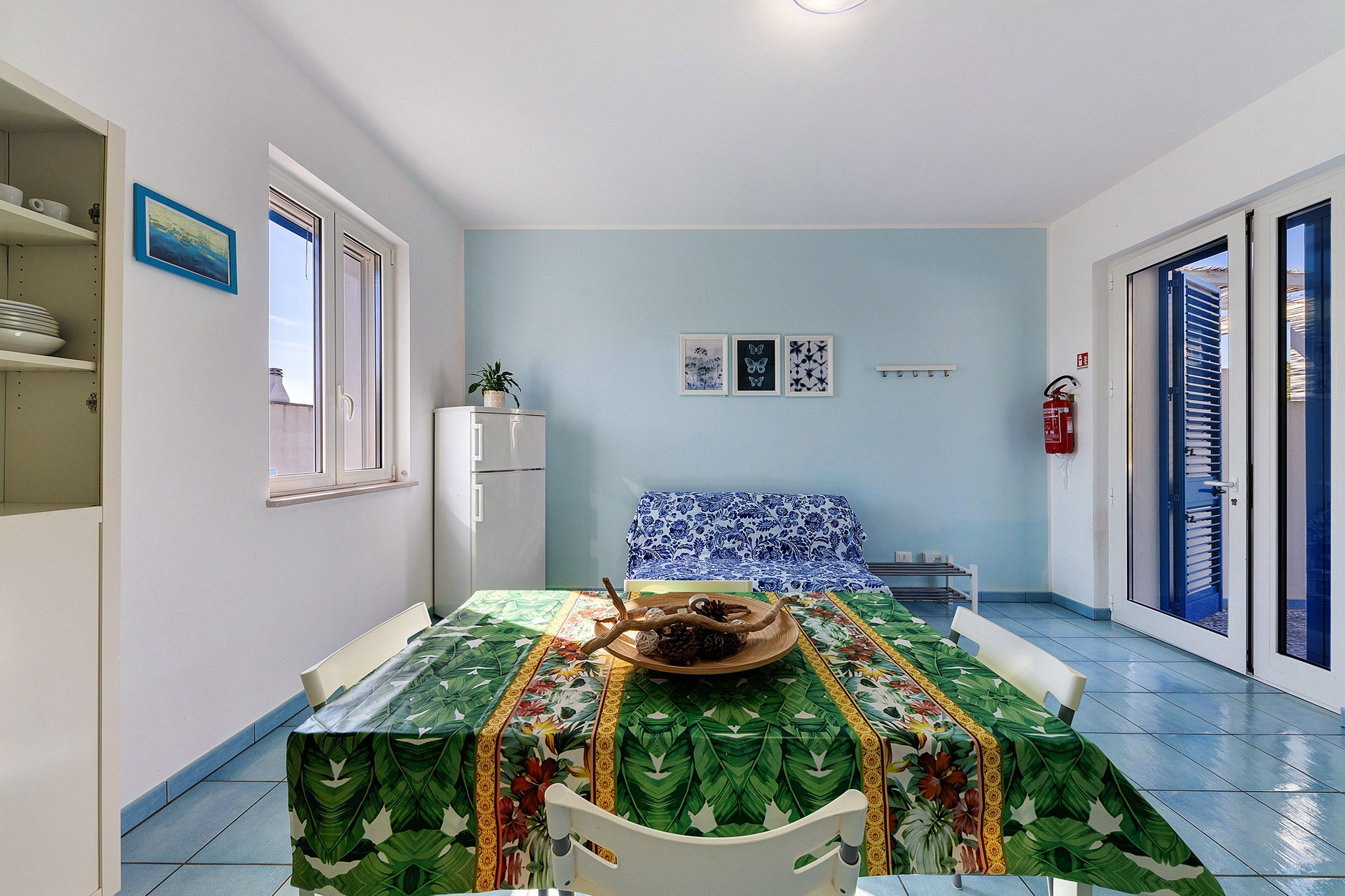 A compact living space with a dining area, a bed with a blue floral bedspread, and a small kitchenette.