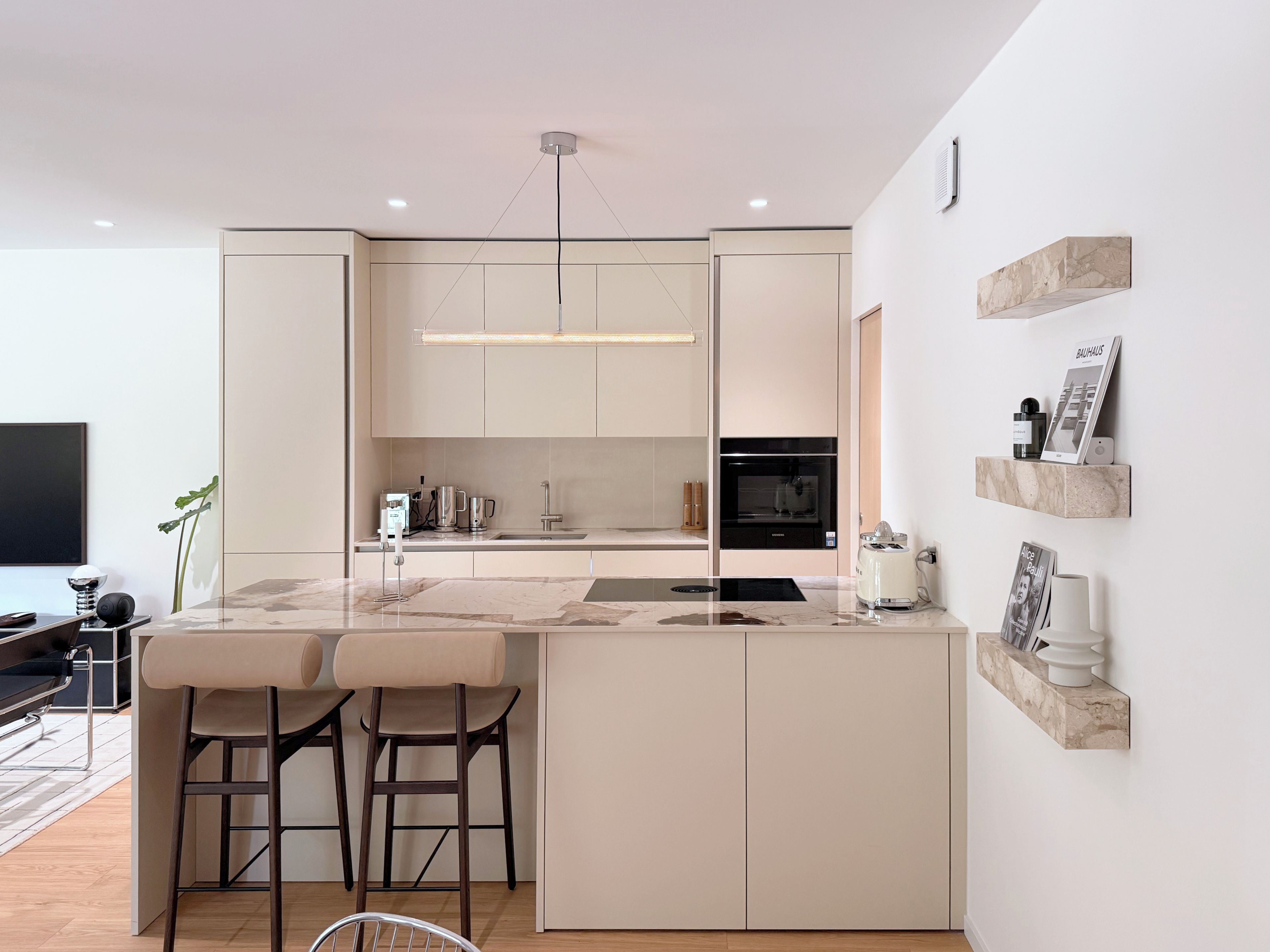 A modern kitchen with a central island, bar stools, a flat-screen TV, and a minimalist design.