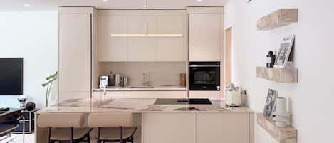 A modern kitchen with a central island, bar stools, a flat-screen TV, and a minimalist design.