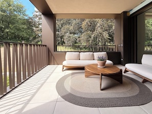 A modern balcony with a sofa, a round wooden table, and a potted plant. - Serenity77 · 100m² designed by an architect, Geneva (Vandœuvres)