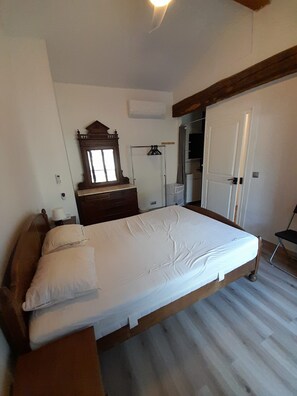 Quarto com cama, cômoda, espelho, guarda-roupa e porta.