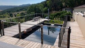 A rooftop pool with a wooden deck, metal railings, and a view of the surrounding landscape. - Vrbo Property (Saint-Ferriol)