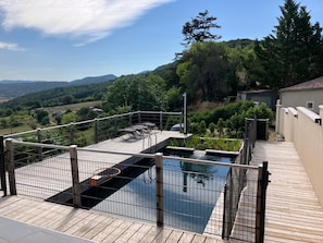 Uma piscina no terraço com deck de madeira, grades de metal e vista para a paisagem ao redor.