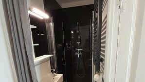 A compact bathroom with a shower, a sink, and a mirror. - Vrbo Property (Saint-Ferriol)
