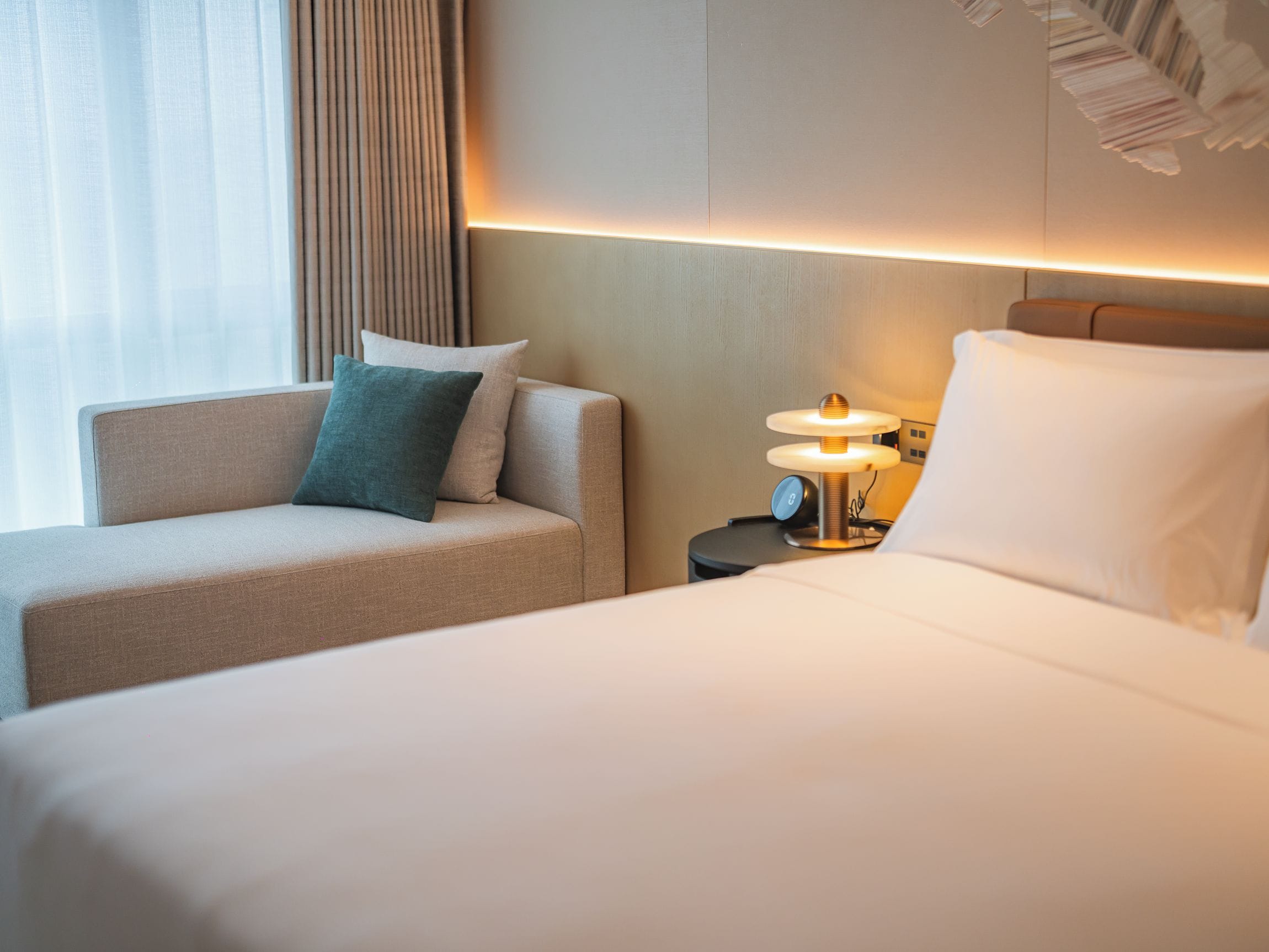 Une chambre d’hôtel avec un lit, un canapé, une table de chevet avec une lampe et une fenêtre avec des rideaux.