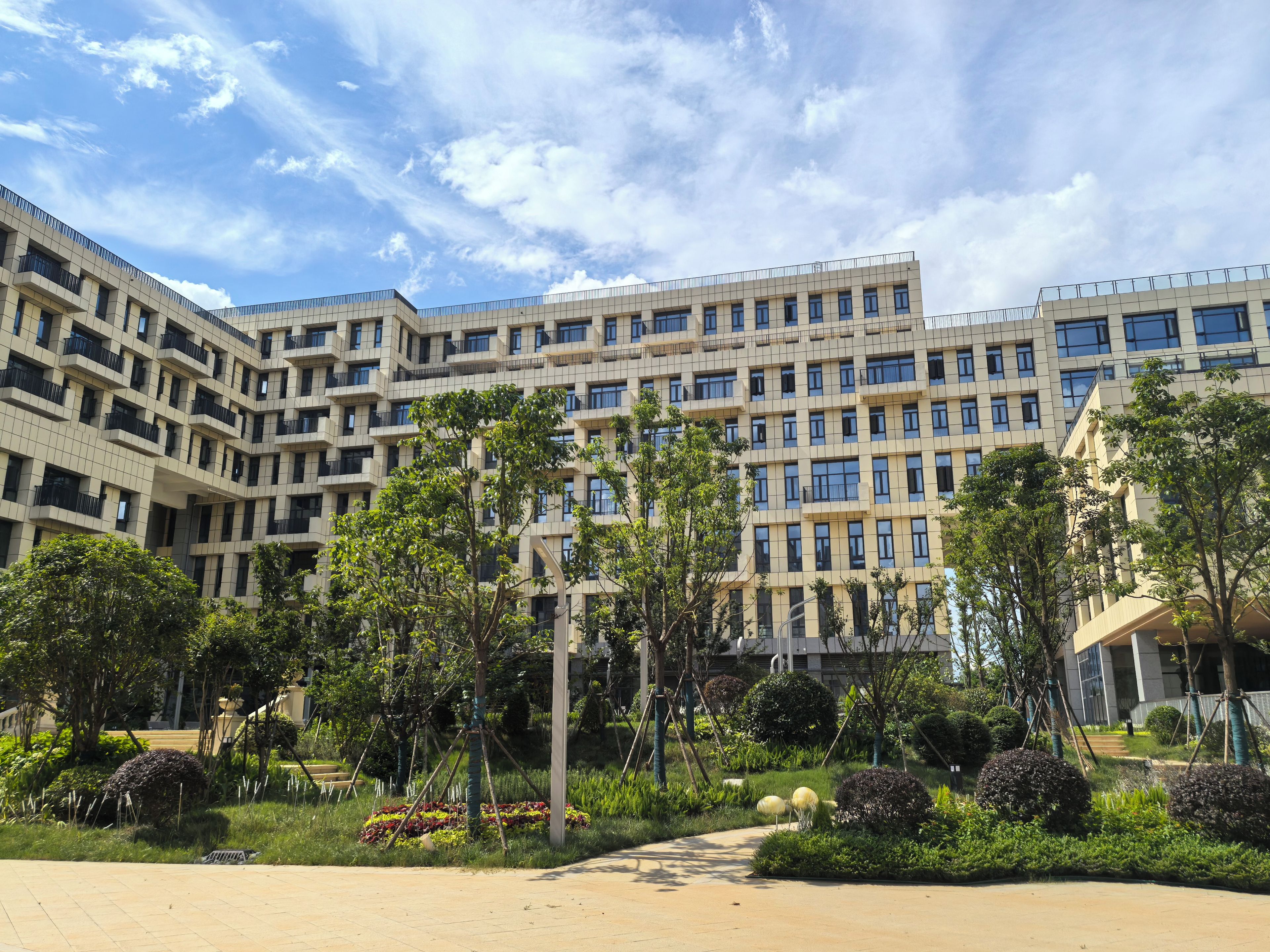Un edificio moderno con varios pisos, rodeado de jardines ajardinados y árboles.