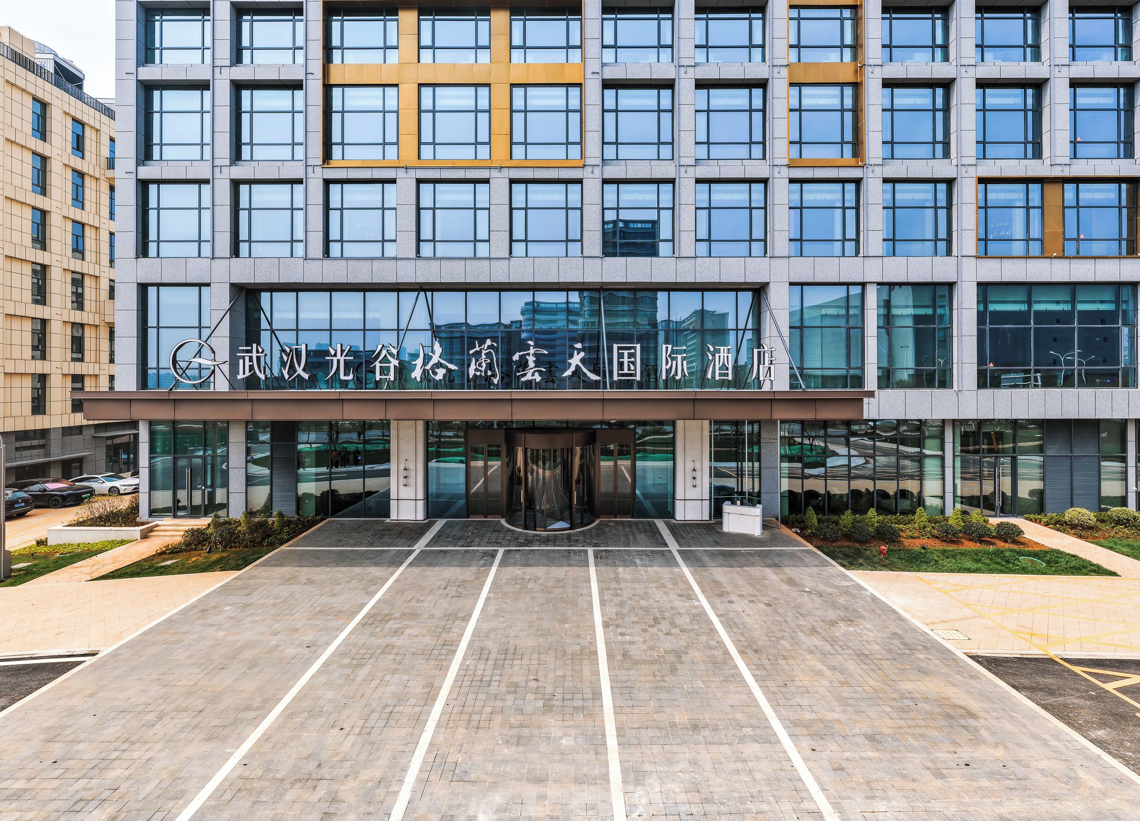 A modern building with a glass facade, a large entrance, and a parking lot.