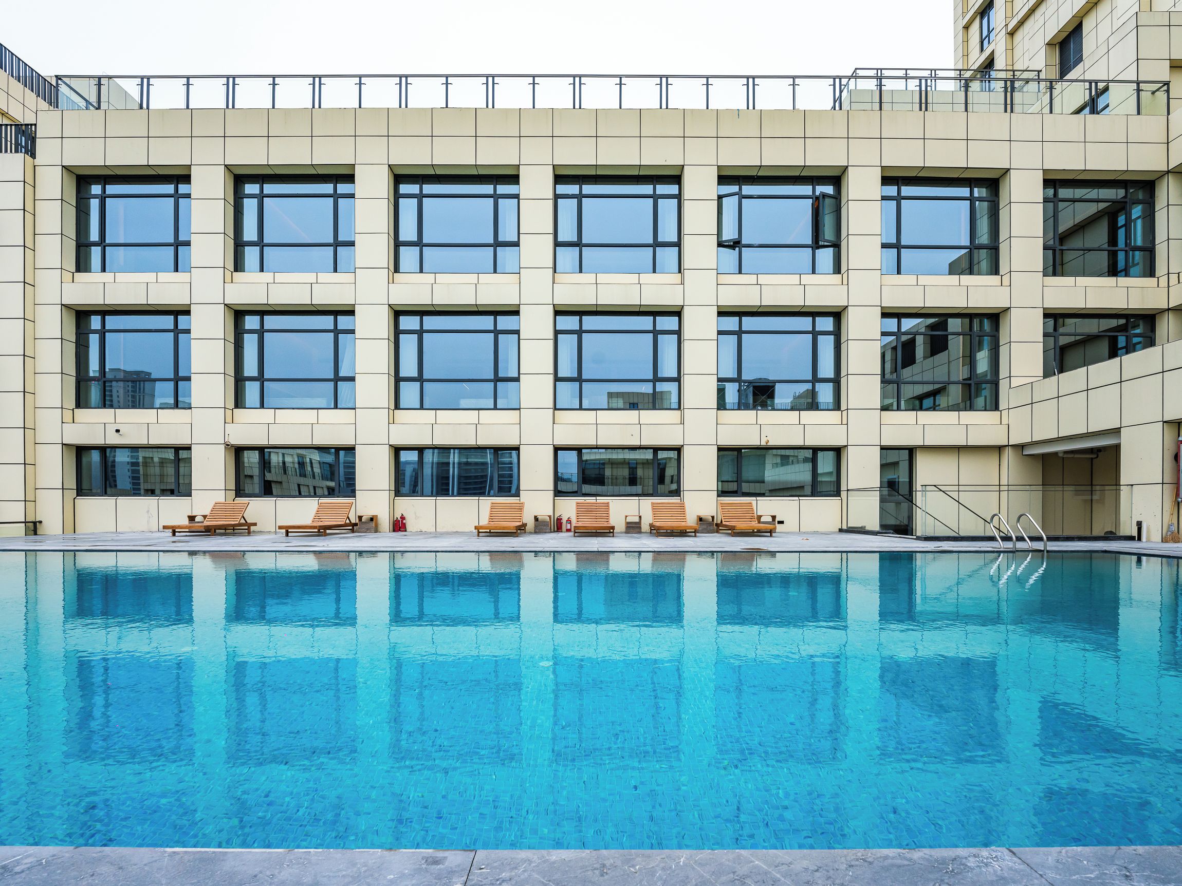 A modern building with a pool, multiple windows, and outdoor seating.