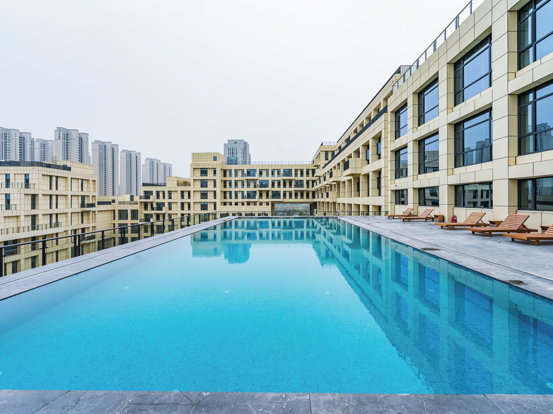 Una piscina con superficie de agua azul cristalina, rodeada de edificios modernos con balcones y ventanas grandes.
